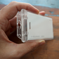 A hand holds the Clear Vertical Permanent Locking Plastic Card Holder (P/N 1840-6045), showcasing its transparent plastic design with a clear sliding cover.