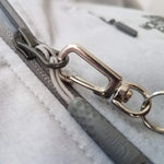 Close-up of a gray backpack zipper with a Custom Retractable Ski Pass Holder - Heavy Duty Sport Reel (2120-4101) - Add Your Logo and small carabiner keychain attached to the zipper pull.