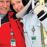 Two people dressed in winter jackets, scarves, and earmuffs hold ski poles. Both have "Vermont Ski Club" badges hanging from their Custom Retractable Ski Pass Holder - Heavy Duty Sport Reel (2120-4101) - Add Your Logo.