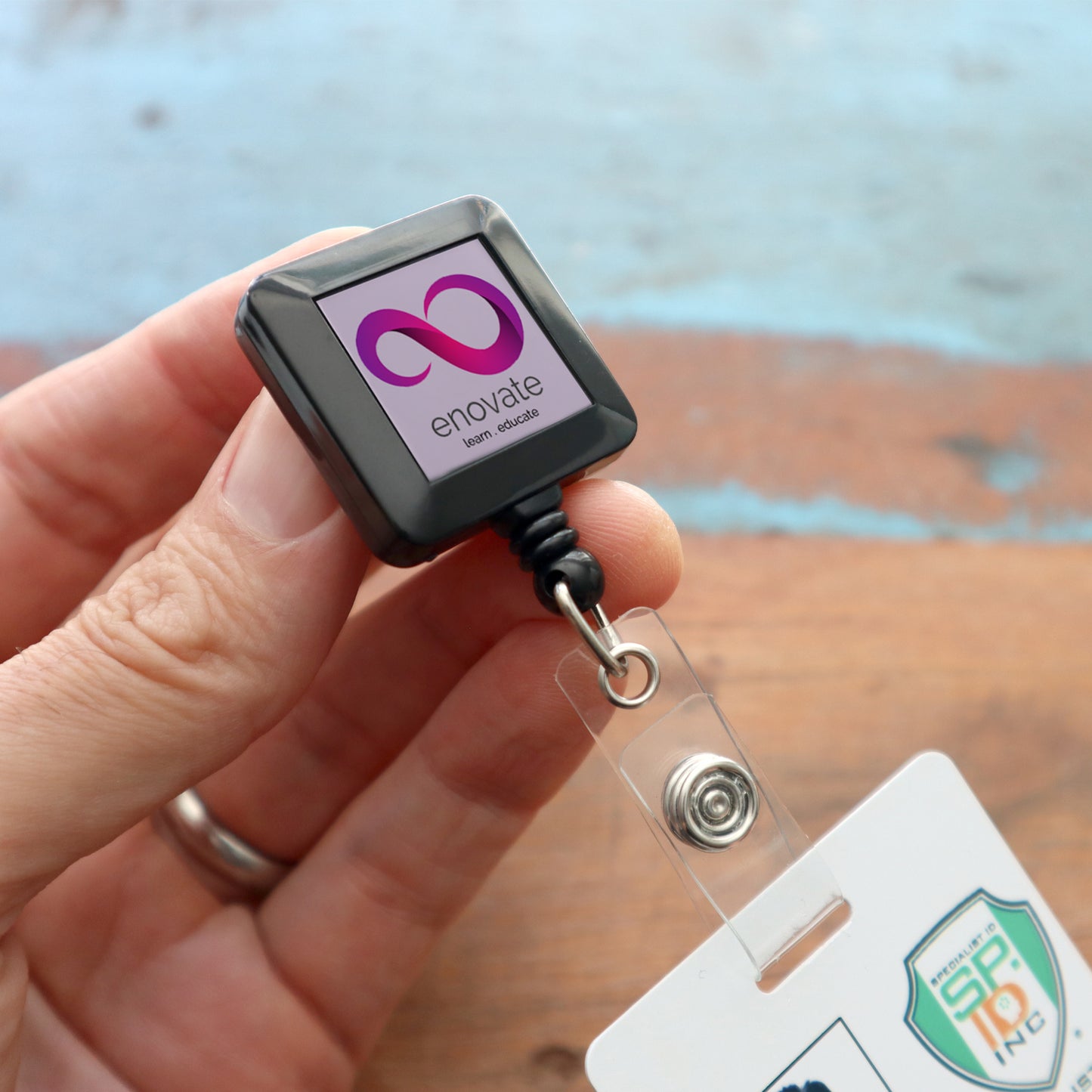 Close-up of a hand holding the Custom Square Retractable Badge Reel with Spring Clip (2120-5701-Custom), displaying a stylish and practical retractable nylon cord alongside a logo-adorned ID card.