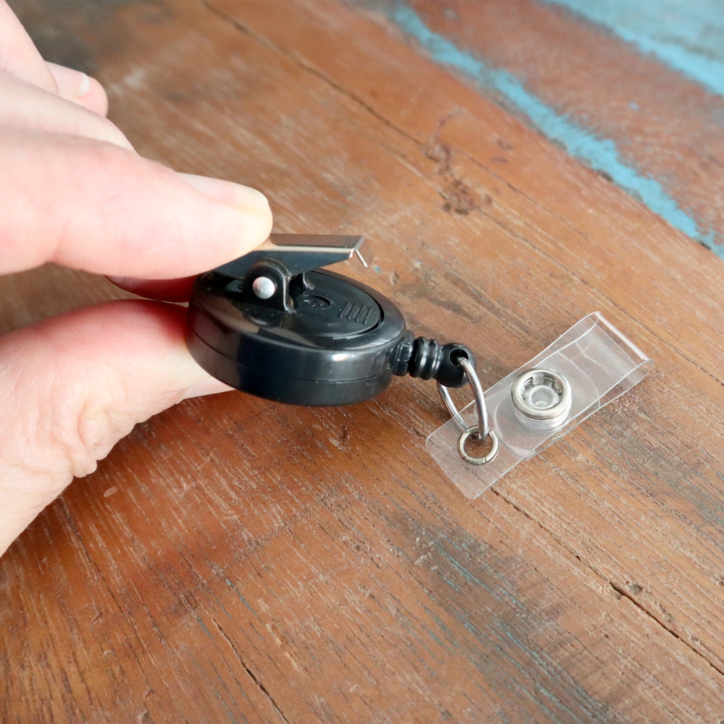 A hand holds the modern Badge Reel with Swivel Spring Clip (P/N 2120-760X), elegantly positioned on a wooden surface.