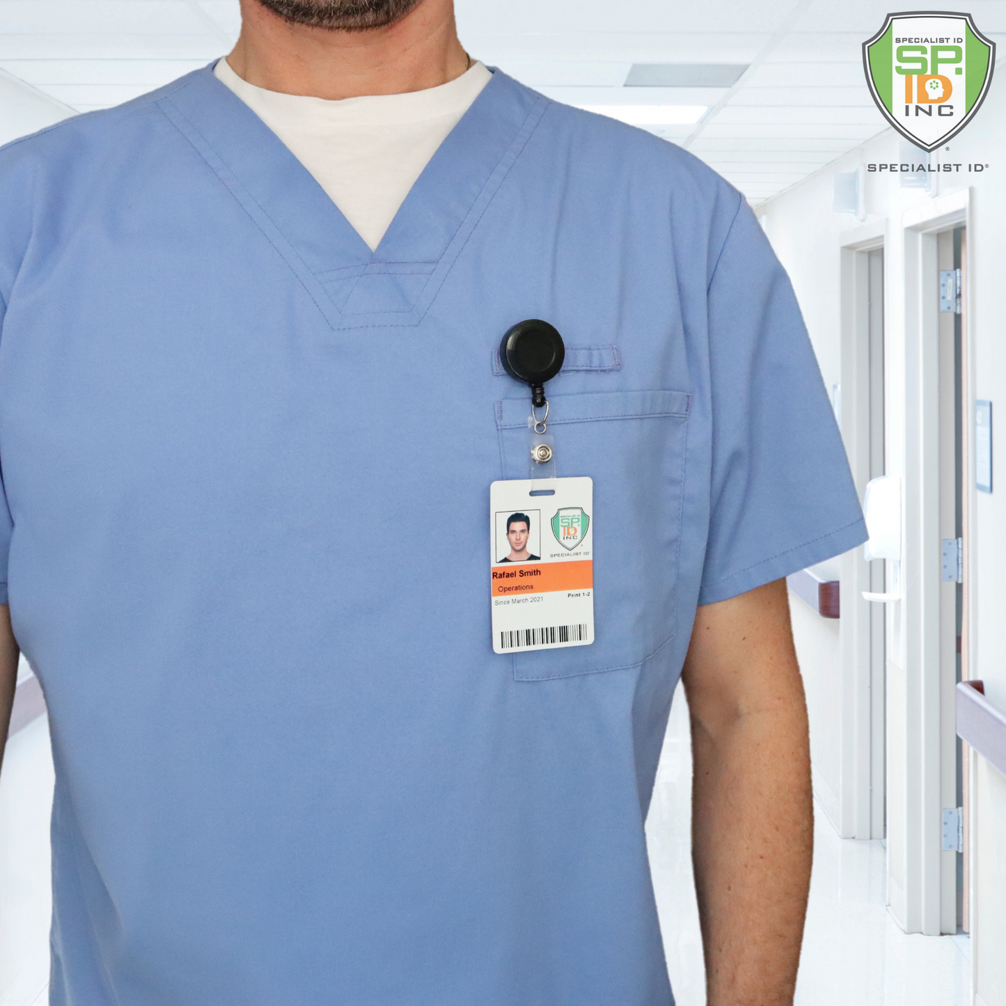 A person in blue scrubs with an ID badge, attached to a Badge Reel with Swivel Spring Clip (P/N 2120-760X), stands in a hospital hallway.