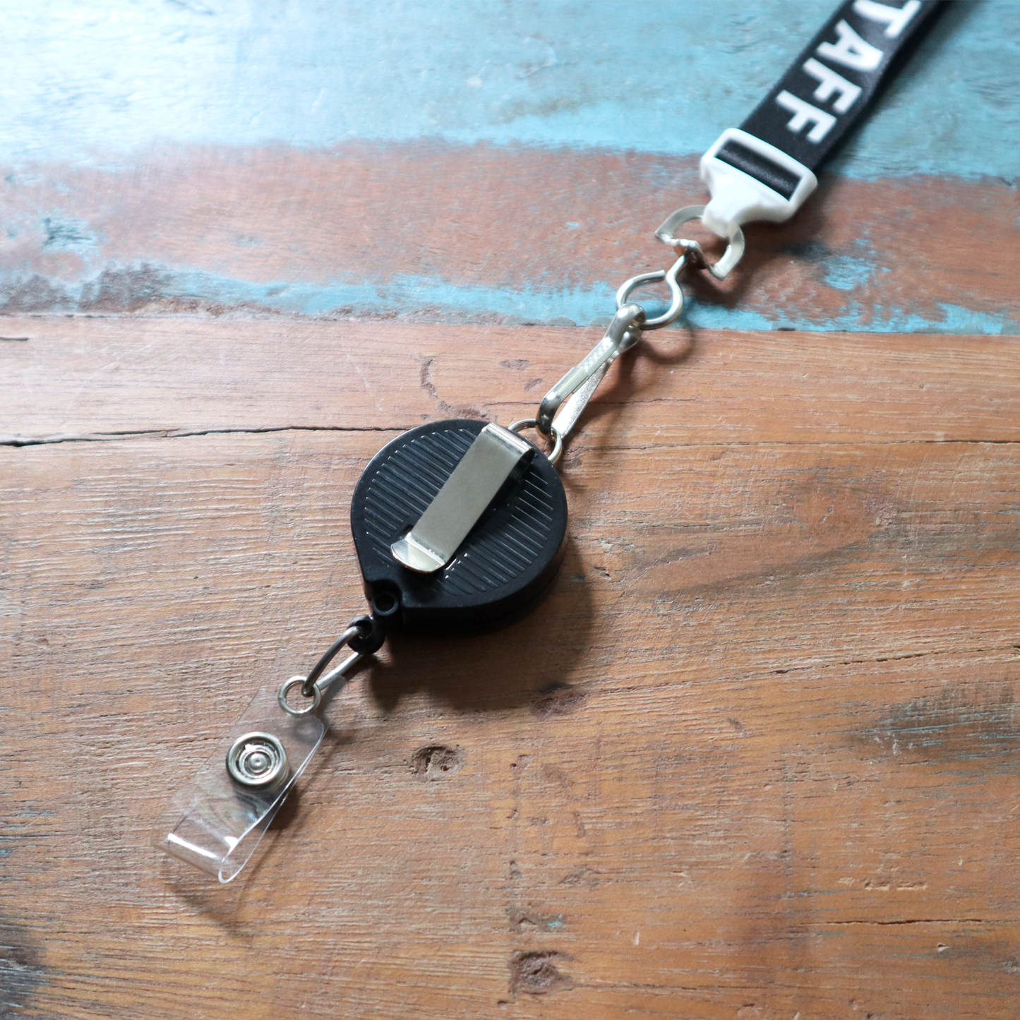 A sleek Badge Reel with Lanyard Attachment and Belt Clip (P/N 2124-302X) featuring a retractable staff holder is seamlessly joined to a lanyard, resting on a wooden surface.