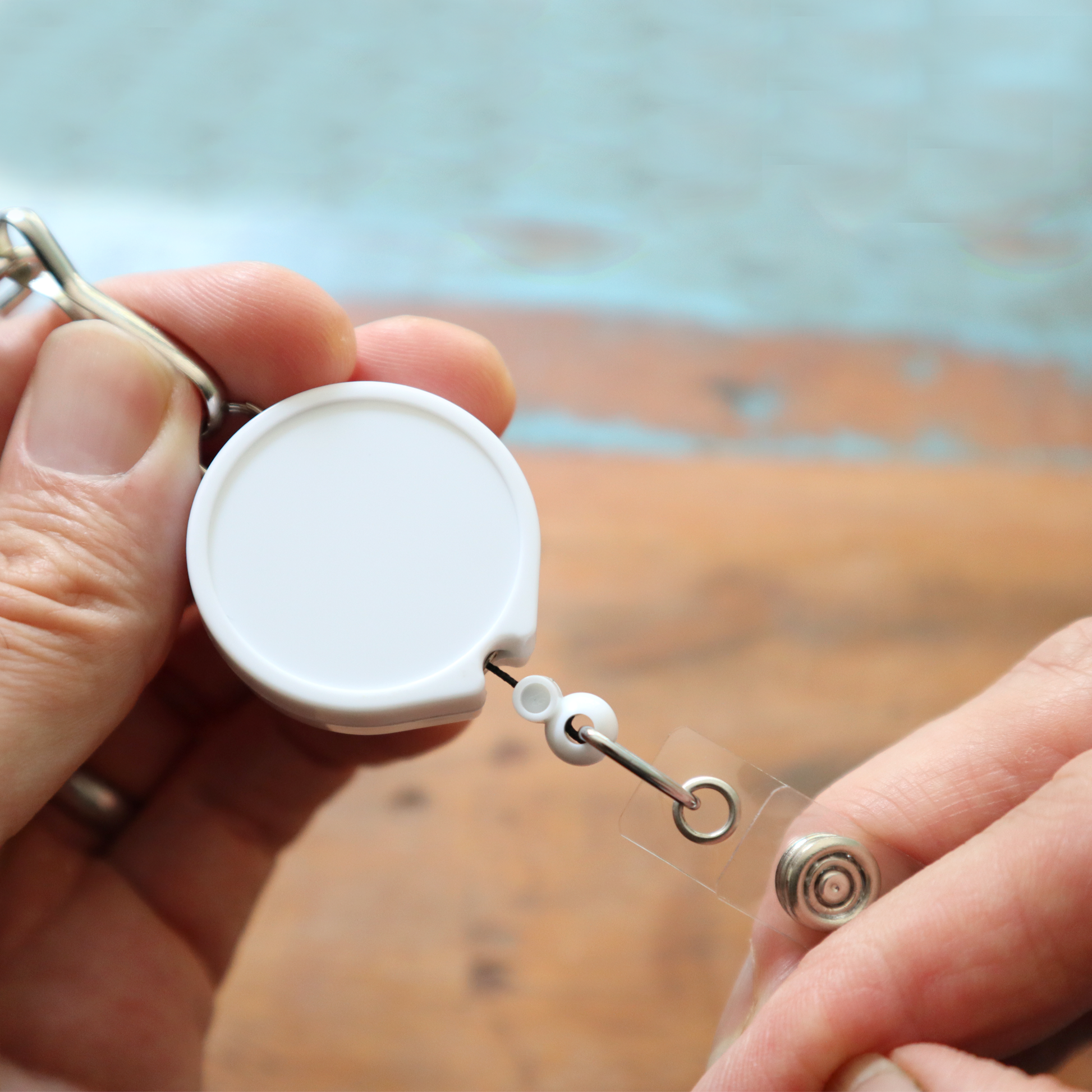 Close-up of hands holding the Badge Reel with Lanyard Attachment and Belt Clip (P/N 2124-302X), which features a metal clip and a transparent string, ideal for attaching to any belt clip.