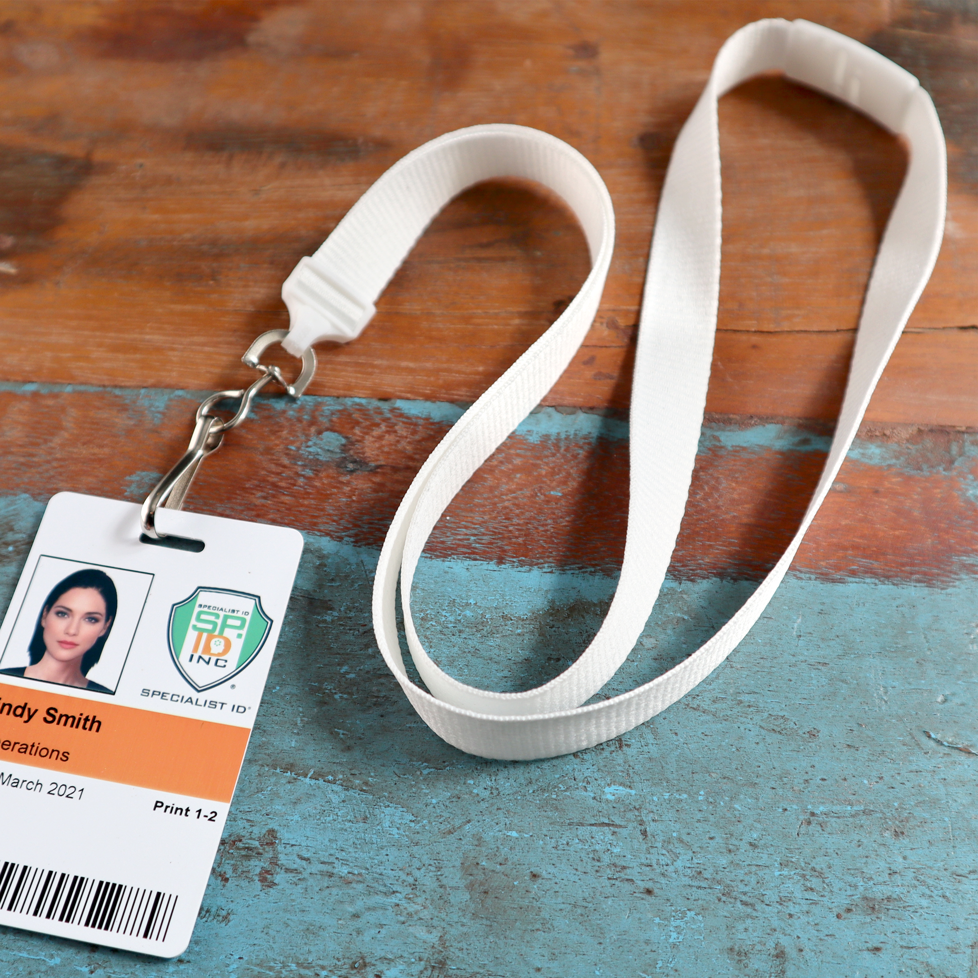 A Flat Wide Breakaway Lanyard with Swivel Hook (2138-500X), measuring 5/8 inches in width, is displayed holding a clipped ID badge. The badge shows a photo, name, company logo, job title, department, and barcode against a rustic wooden background.