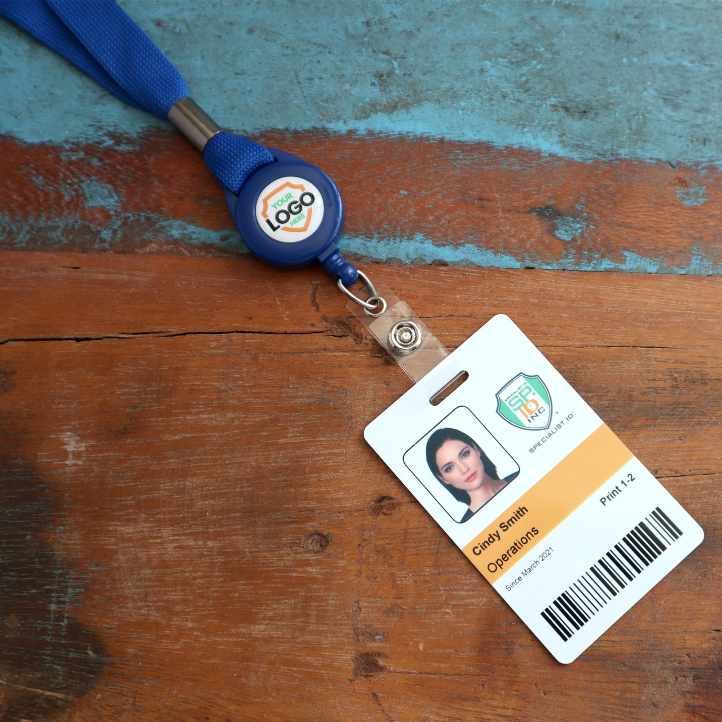 A photo of an identification badge on a worn wooden surface. The badge, held by one of our Breakaway Lanyard with Custom Badge Reel Combo - Add Your Logo to Customize, includes a headshot, the name "Cindy Smith," and the word "Operations" along with other identification details.