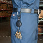 A person wearing blue Dickies work pants with a black belt attached to a Key-Bak Heavy Duty Badge Reel Carabiner with Key Ring and 48" Cord (488B-HDK), featuring multiple keys hanging from it. The background includes shelves with boxes in a warehouse.