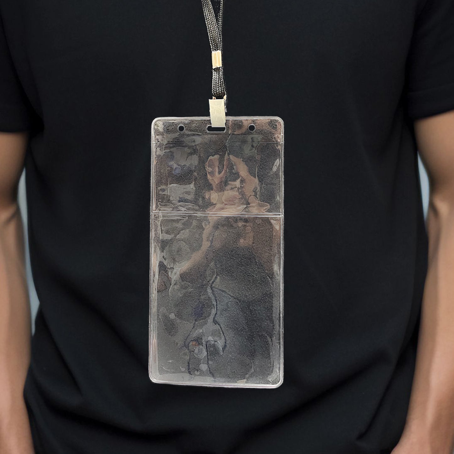 A person wearing a black shirt with a Clear 4" X 7 1/2" Vinyl Vertical Large Badge Holder With Two Pockets (P/N 1840-5052) hanging from a black lanyard around their neck.