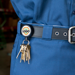 A set of keys attached to a Customizable Key-Bak Mid Size Key Ring Badge Reel with Belt Clip (#6) - Add Your Logo on the belt of a person wearing a blue uniform. The badge holder, which can be customized to promote brand awareness, has a placeholder for a logo.