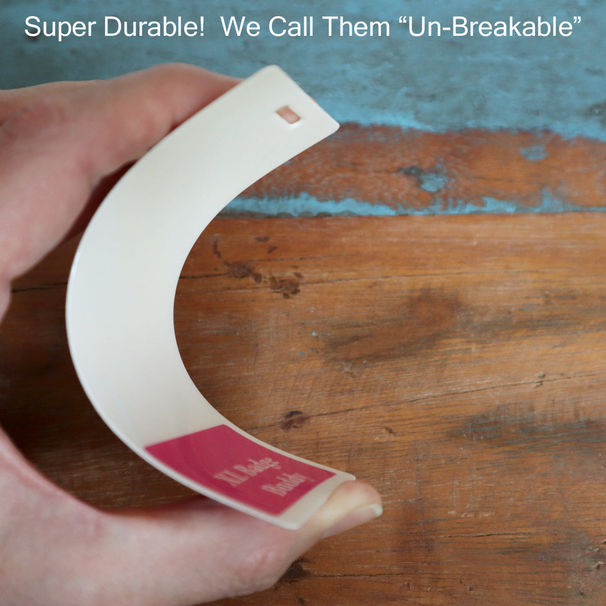 A hand bends a thin, durable white plastic sheet with a pink label. Text at the top reads, "Super Durable! We Call Them 'Un-Breakable'". Perfect for your Oversized RN Badge Buddy - Extra Large Badge Buddies for Registered Nurse - Vertical Hospital ID Badge Backer!