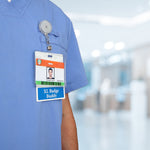 A person in blue scrubs wears an ID badge with a photo, accompanied by an Oversized Custom Printed Horizontal XL Badge Buddy (Extra Large Size) underneath. The background reveals a blurred indoor setting, emphasizing the importance of ID badge recognition.