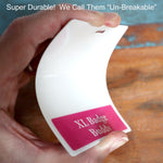 A person bends a white plastic badge with a pink label that reads "Oversized Custom Printed Horizontal XL Badge Buddy (Extra Large Size)." The text above says, "Super Durable! We Call Them 'Un-Breakable'". Perfect for ID badge recognition, this extra large horizontal custom printed badge buddy ensures your identification stands out.
