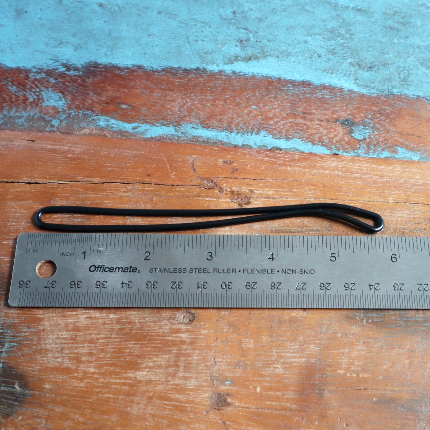 A stainless steel ruler marked with both inches and centimeters rests on a wooden surface, accompanied by 6" Plastic Luggage Tag Loop Straps in Solid Colors - Red, Green, Black, Blue & White (2410-200X) placed parallel to it, resembling one of those travel accessories you find in luggage worm loops.