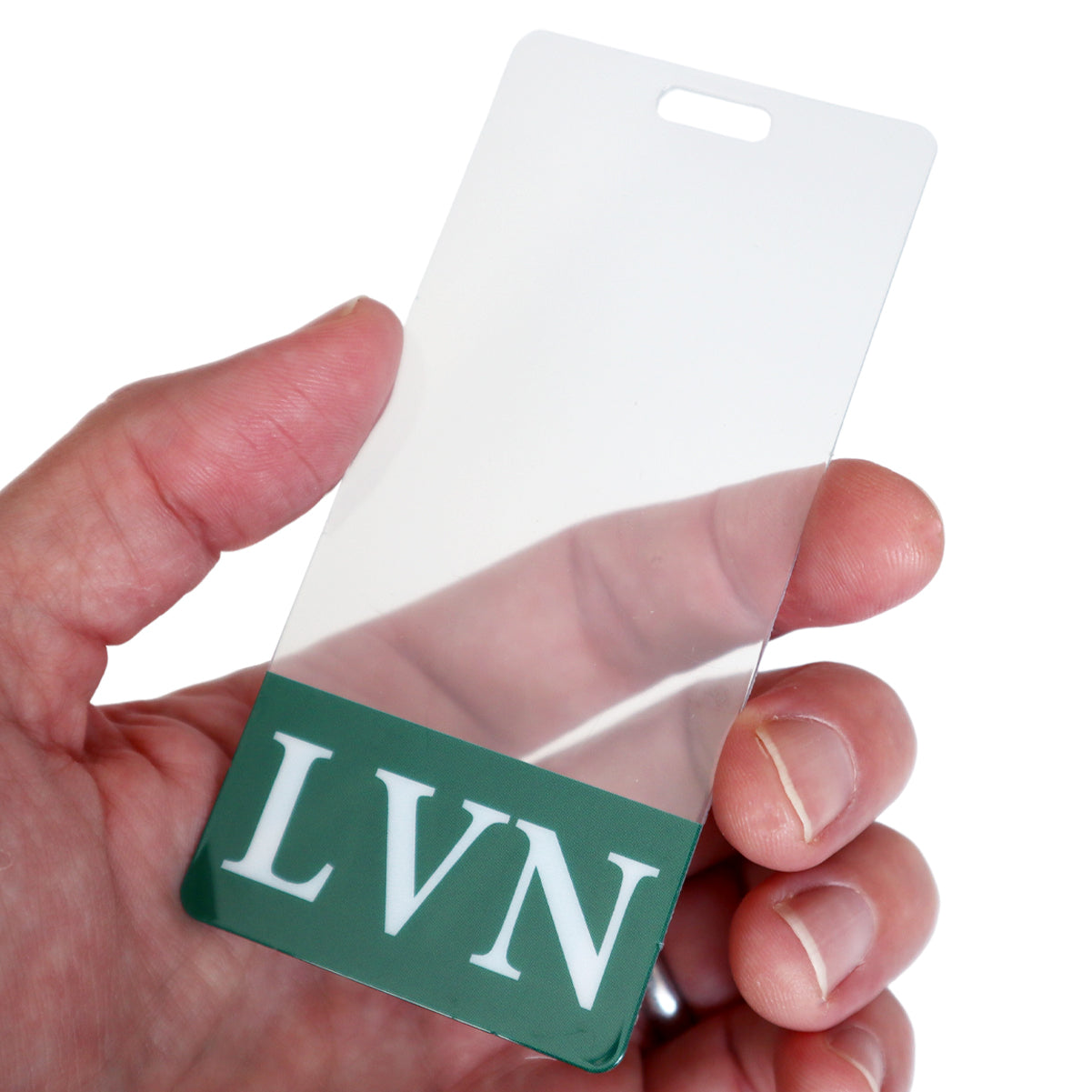 A close-up of a hand holding a Clear LVN Badge Buddy Vertical with Green Border for Licensed Vocational Nurses, displaying the initials "LVN" and a green section at the bottom, typical for licensed vocational nurses.