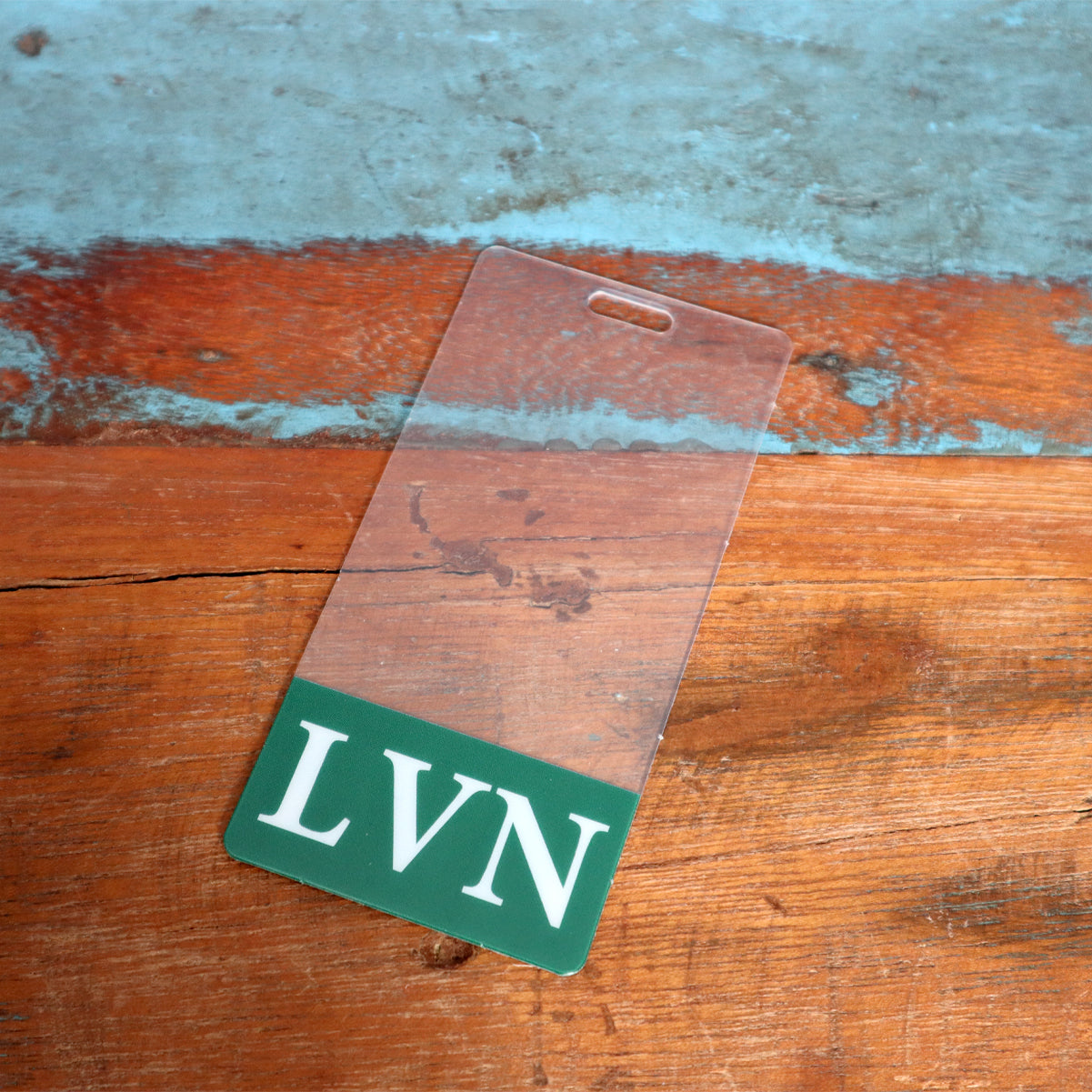 Clear LVN Badge Buddy Vertical with Green Border for Licensed Vocational Nurses, placed on a weathered wooden surface, resembling a vertical ID badge ideal for licensed vocational nurses.