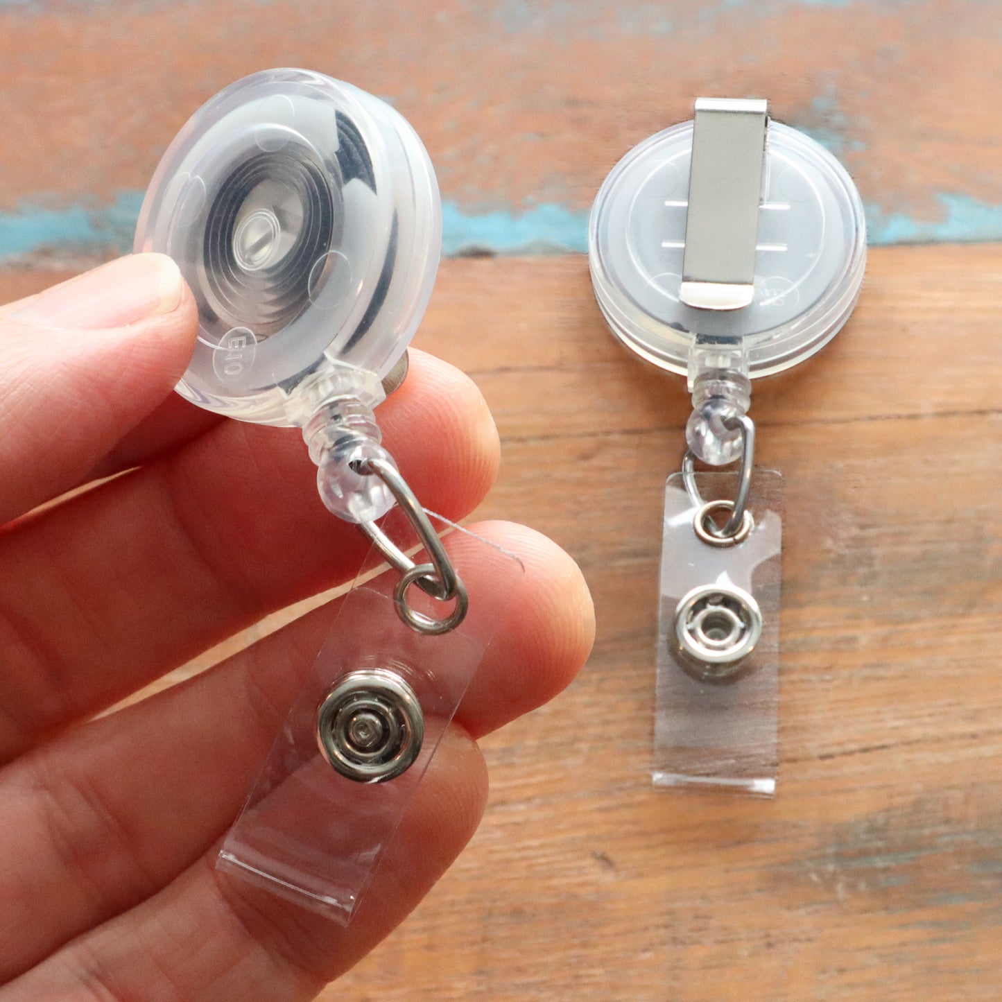 Close-up of a hand holding the Translucent Clear Retractable Badge Reel with Belt Clip (2120-360X) next to another showing the attachment mechanism.