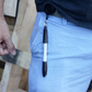 A person in light blue pants has a sleek pen secured with the Retractable Pen / Pencil Holder, featuring a ratcheting "Stay Open" pull cord and belt clip from SPID-3220, elegantly attached at their hip.