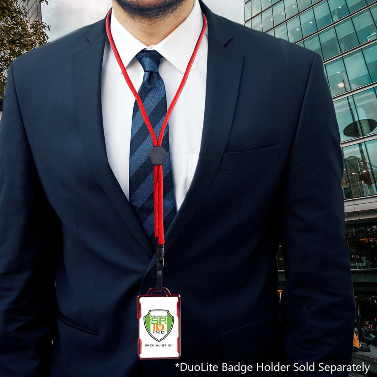 A person wearing a black suit and blue tie with a red lanyard holding an ID badge stands against the backdrop of a glass building. The lanyard, equipped with a breakaway clasp, ensures safety and convenience. Text at the bottom reads, "*Metal Detector Friendly Heavy Duty Custom Lanyard with Diamond Slider, Breakaway Clasp & Quick Release Plastic Hook - MRI Safe (2135-45XX) Sold Separately".