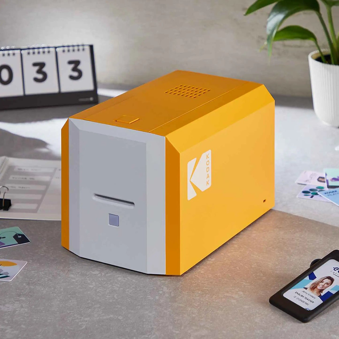 The Kodak ID100S Single-Sided Photo ID Card Printer, with its distinctive rectangular design featuring orange sides and a white front with a slot and small square button, is crafted for efficiency. Measuring 119mm (7.0") in height and 168mm (6.6") in width, this device is well-suited for manual hand-fed printing tasks.