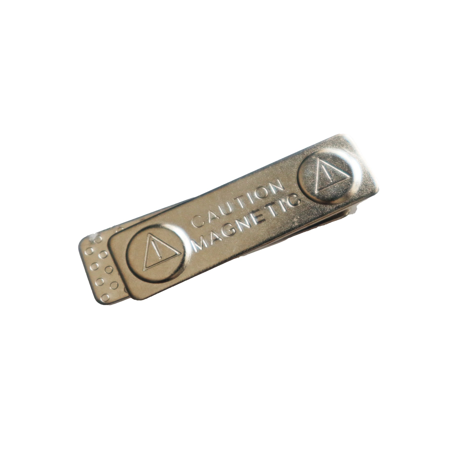 A silver Magnetic ID Badge Holder Sticky Back (P/N 5730-3000) with a triangular logo and "CAUTION MAGNETIC" text embossed on it, this versatile device can also function as a magnetic ID badge holder.