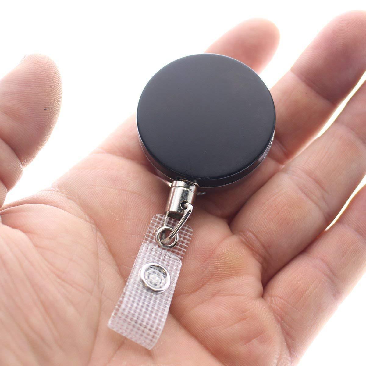 A hand holding an Heavy Duty Badge Reel With Steel Cable 2120-3305, featuring a black round retractable design with a clear plastic strap and metal snap button.
