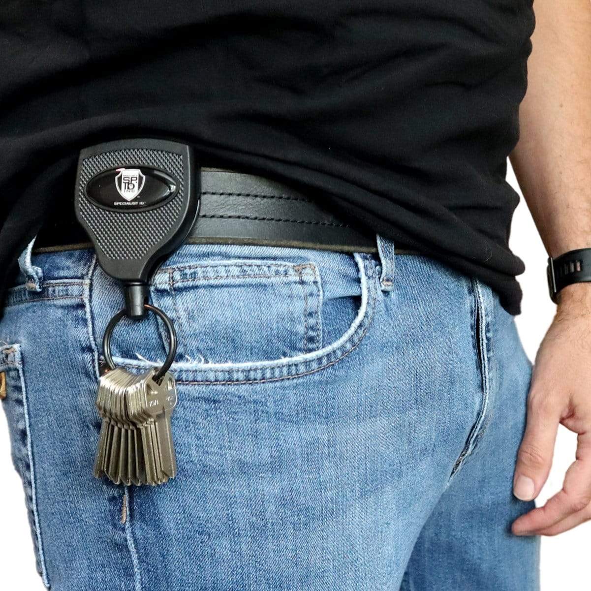 A person wearing blue jeans and a black shirt shows a set of keys attached to a Super Heavy Duty Retractable Keychain - 8oz or 10 Keys - Durable 48” (4 Ft) Kevlar Lanyard.