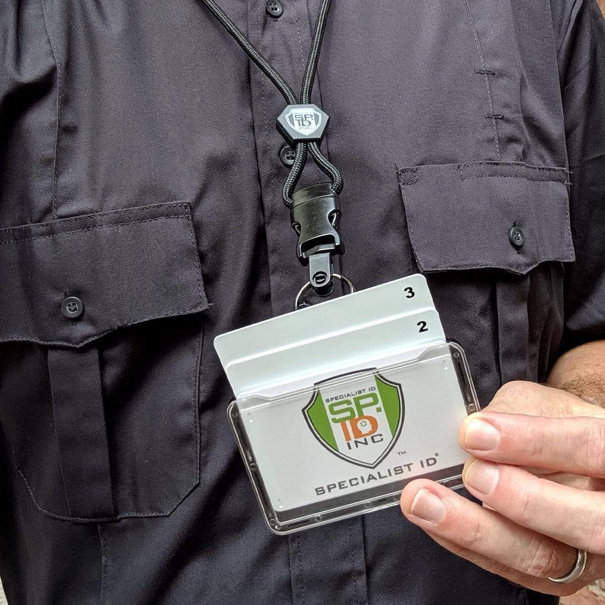 Person holding a Specialist ID Horizontal 3 Card Badge Holder & Heavy Duty Lanyard with Breakaway Clip and Key Ring - Hard Plastic Rigid Name Tag Protector - Top Load for Three Badges, wearing a black shirt and professional work wear.